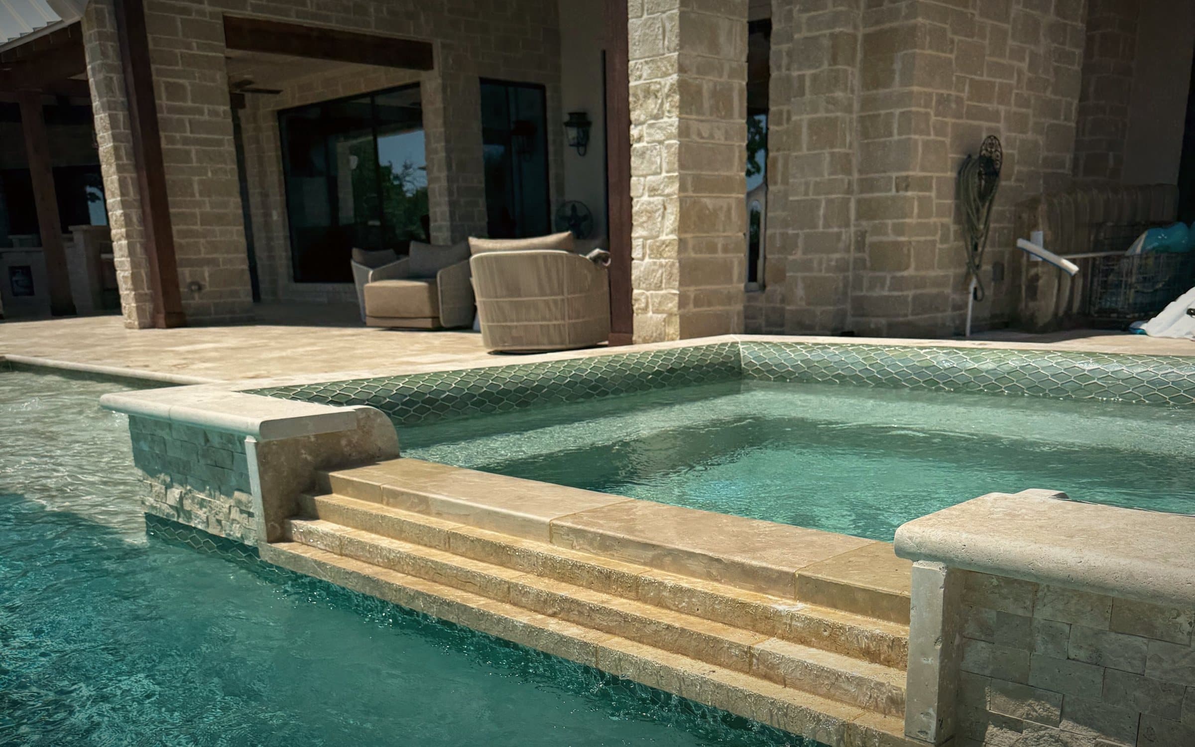 Limestone spa steps spilling into a turquoise pool beside a stone home